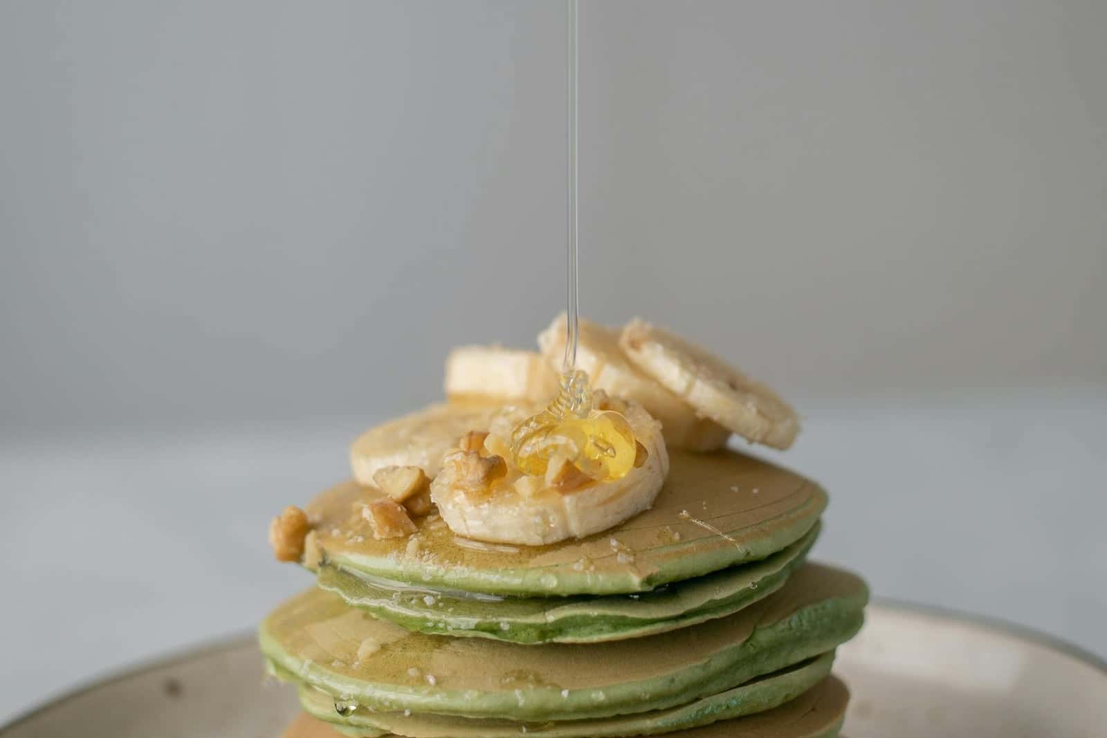 Banana protein pancakes stacked with banana slices and honey on a plate