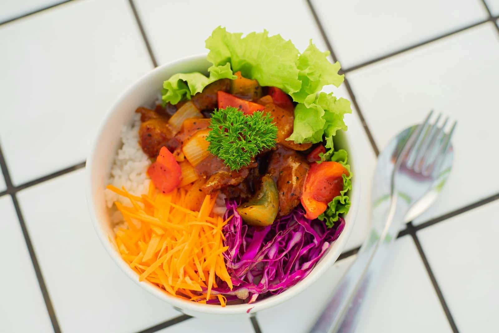 Mango chicken rice bowl with colorful vegetables, greens, and chicken in a white bowl