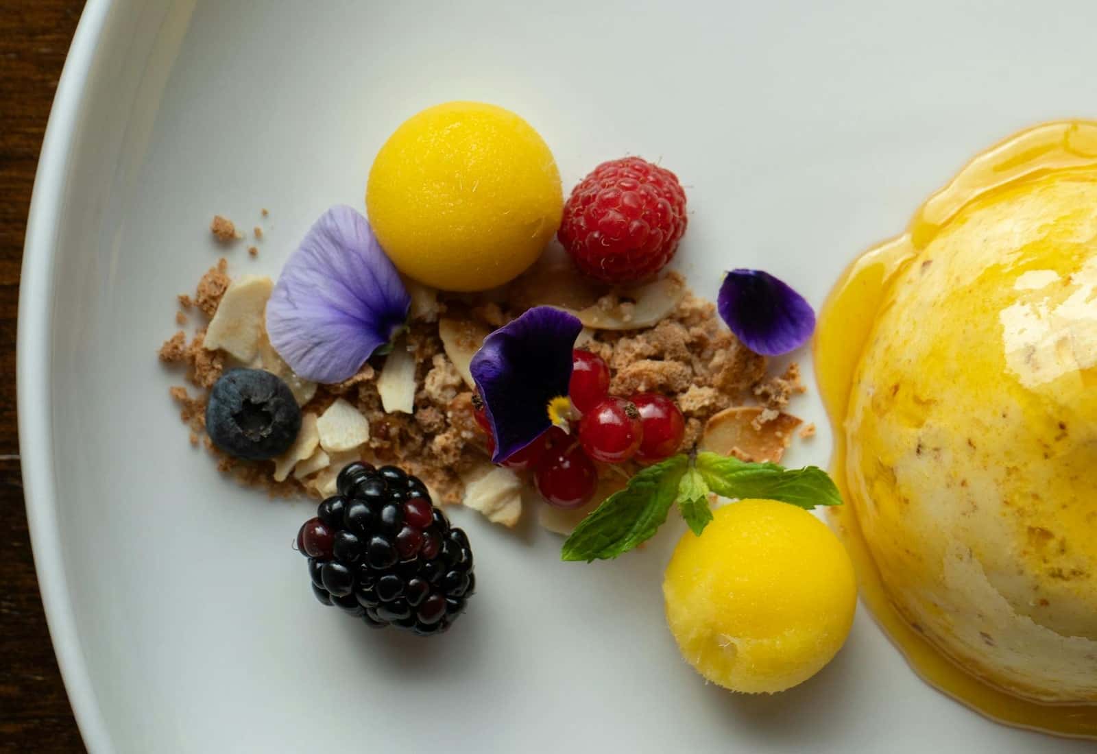 Mango sorbet dessert with bright yellow scoops, berries, and edible flowers on a plate