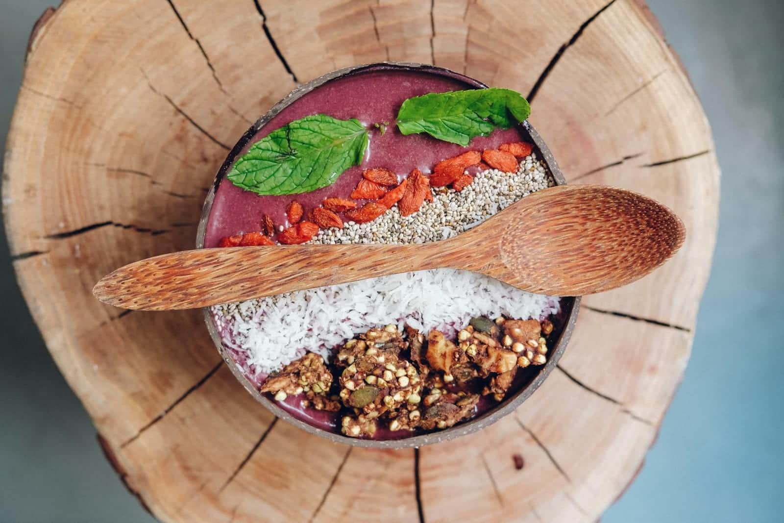 Acai protein bowl topped with granola, berries, chia seeds, and mint in a wooden bowl