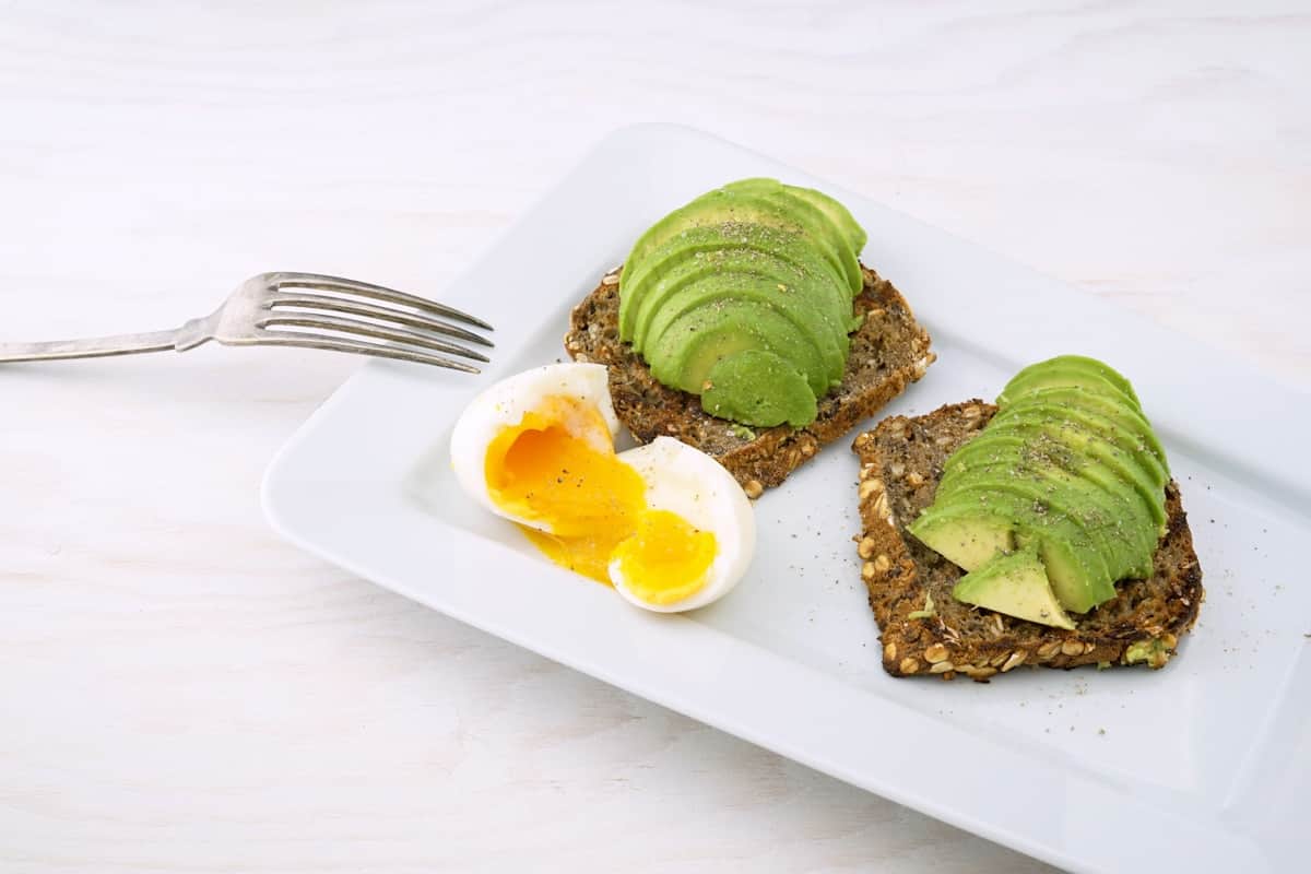 Avocado toast variations with sliced avocado and soft-boiled egg on seeded bread