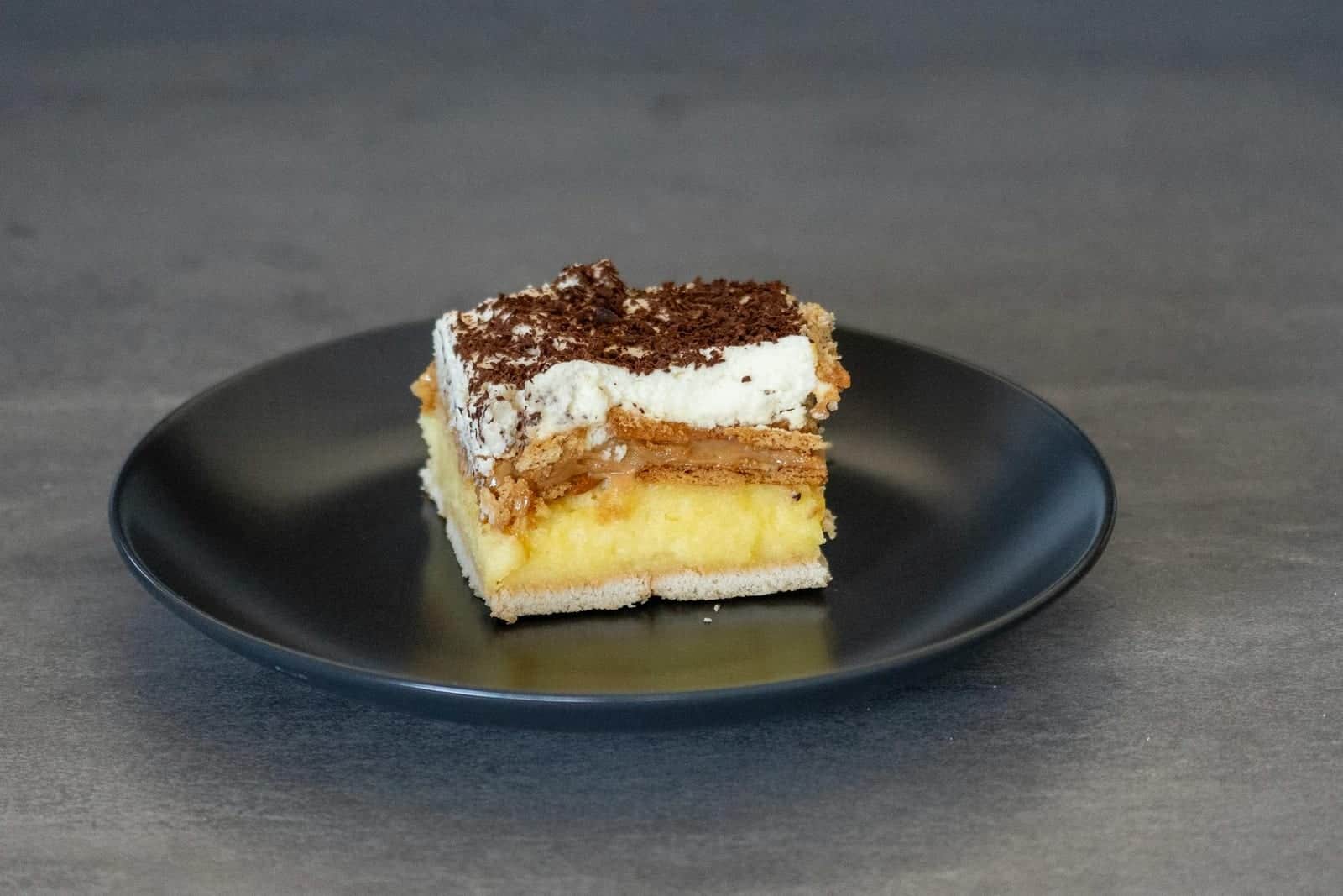 Boston cream pie-style cake slice with custard layer and chocolate topping on a black plate