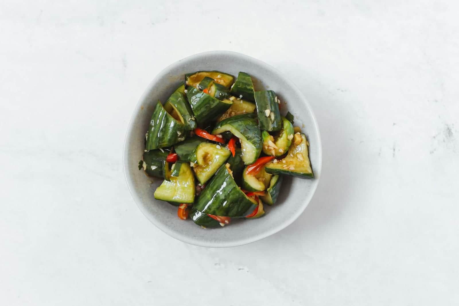 Chinese smashed cucumber salad with cucumber chunks, peppers, and dressing in a white bowl