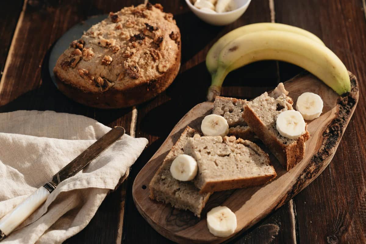 Classic banana bread loaf sliced on a wooden board with fresh banana pieces