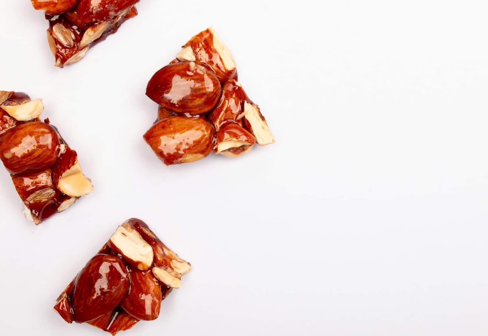 Classic peanut brittle candy pieces with glossy caramel and roasted peanuts on a white surface