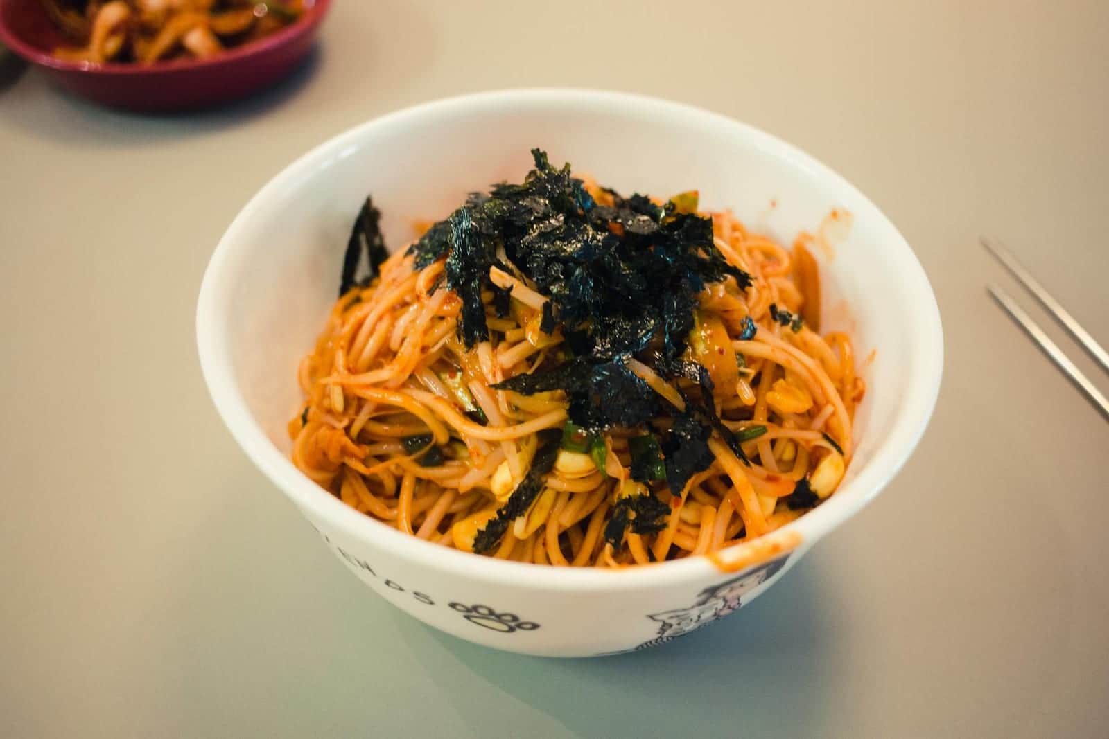 Spicy cold sesame noodles in a white bowl topped with seaweed and sesame