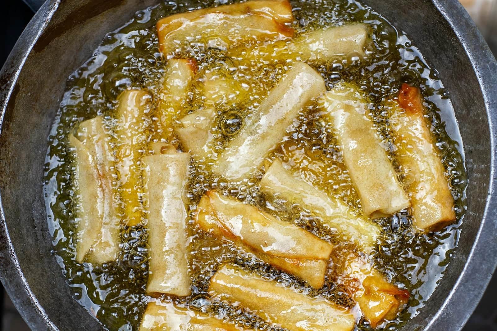 Crispy pork spring rolls frying until golden with bubbled wrappers