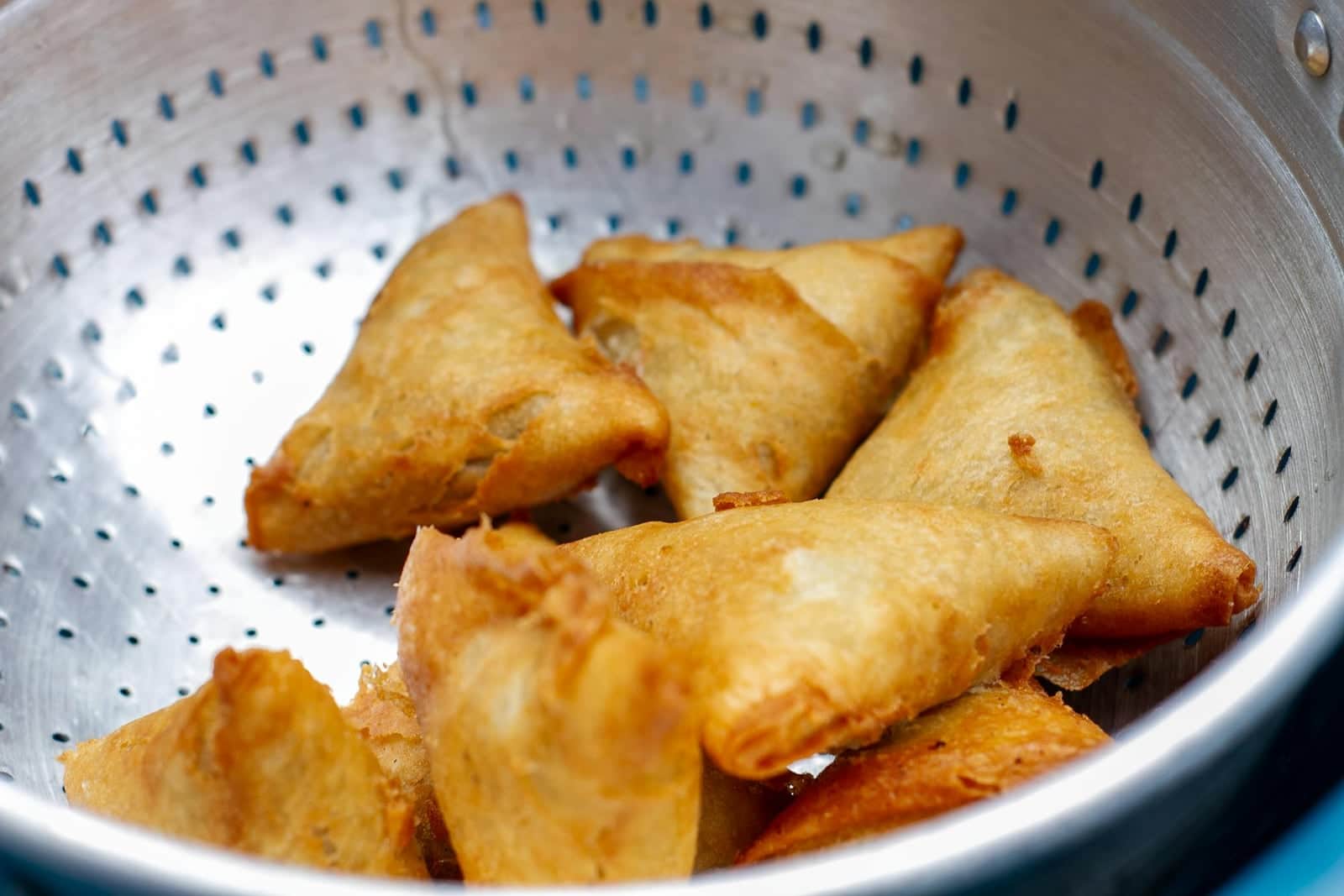 Crispy vegetable samosas cooling in a colander with golden fried pastry