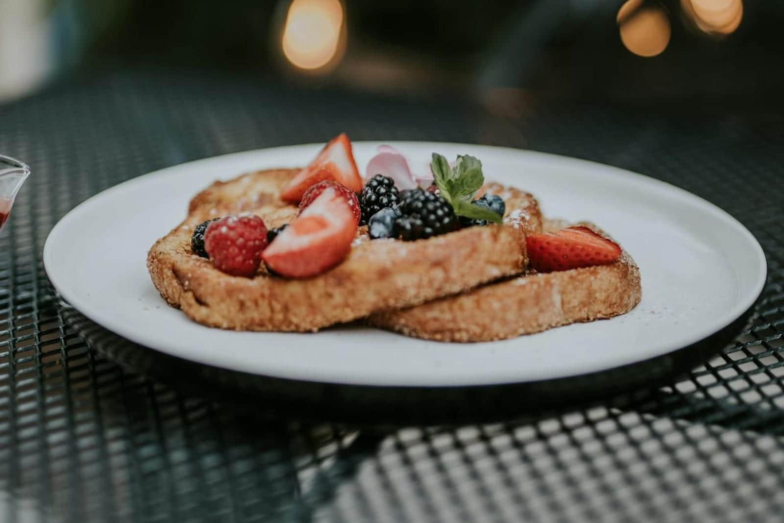 Croissant French toast topped with strawberries, blackberries, and cream on a white plate