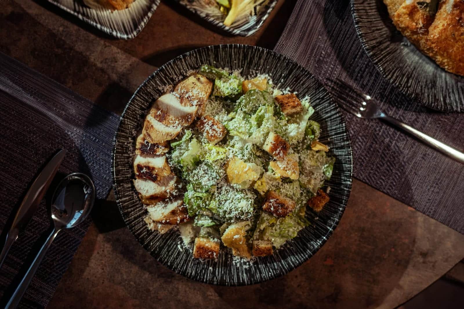 Grilled chicken Caesar salad with romaine, croutons, and parmesan in a dark bowl