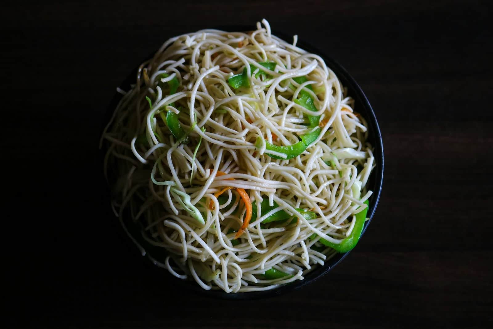 Hakka noodles stir-fried with vegetables and served in a dark bowl
