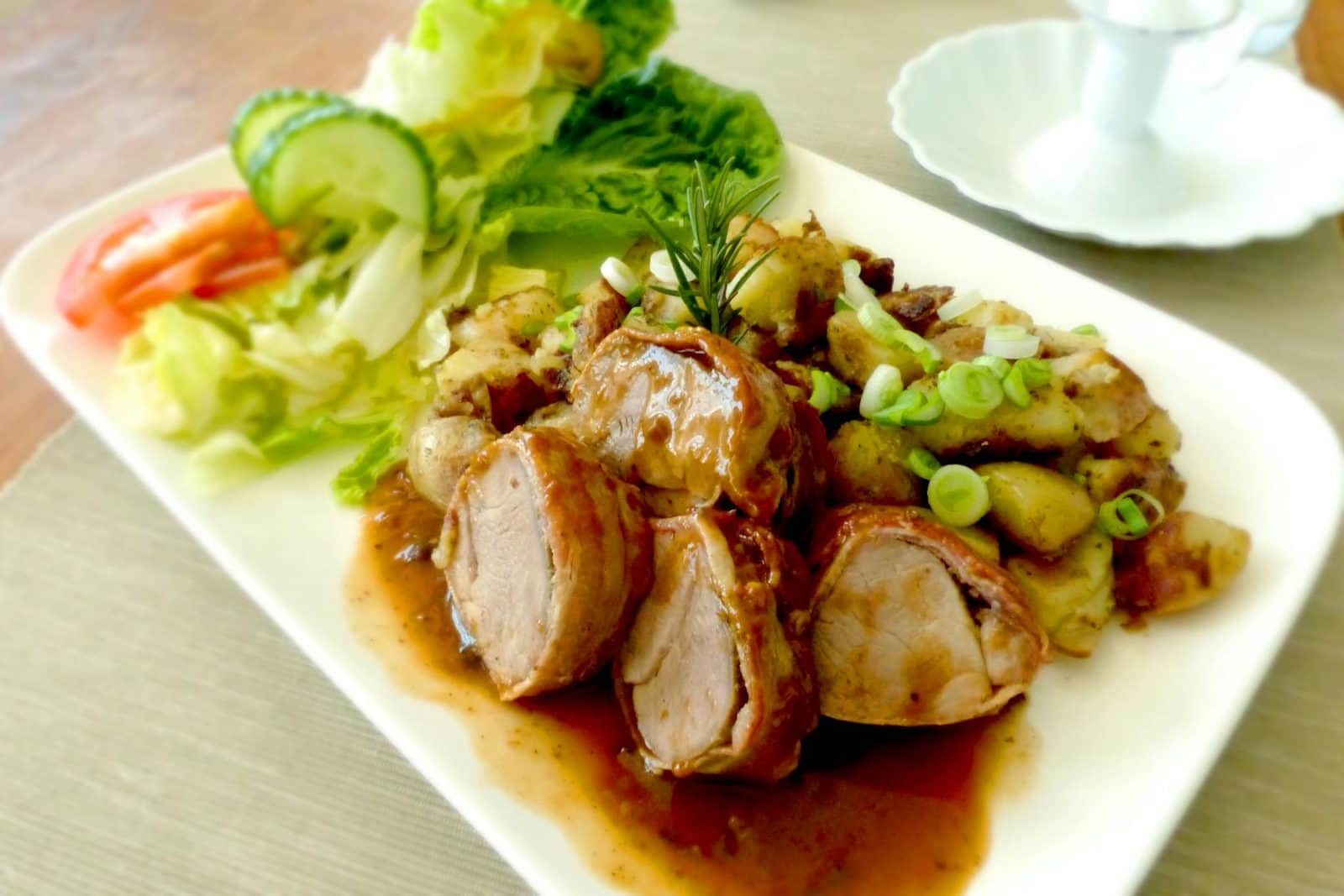 Herb-roasted pork tenderloin sliced with potatoes, rosemary, and a fresh salad
