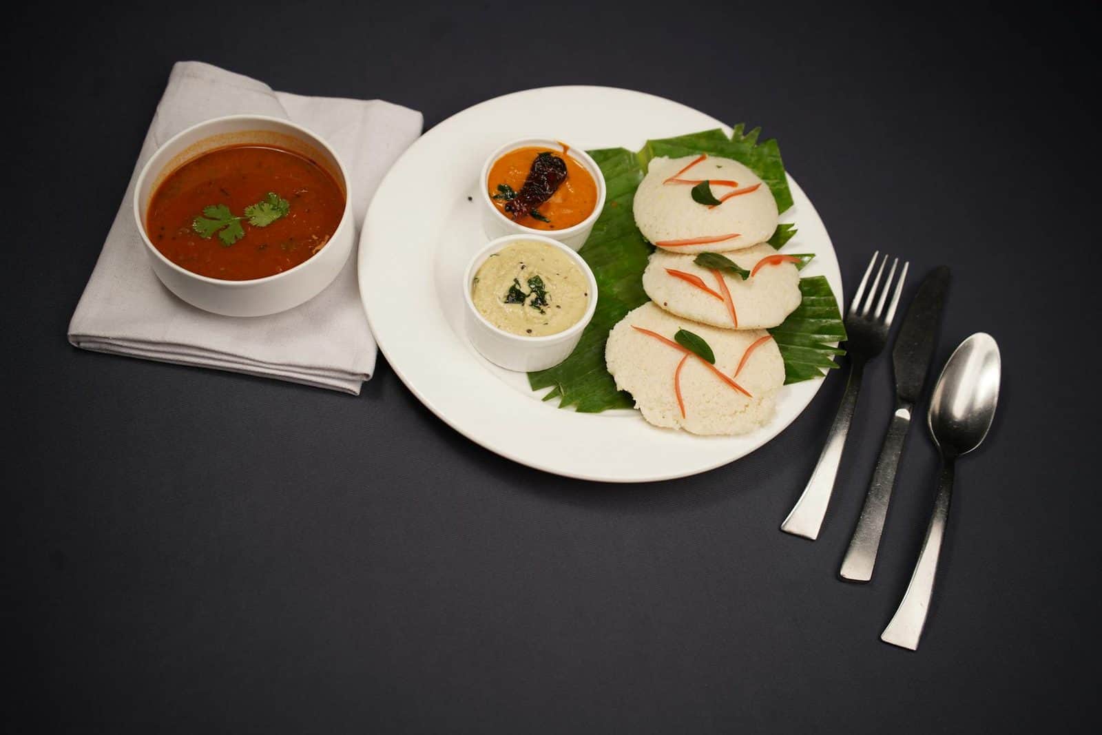 South Indian idli served with sambar and chutneys on a dark plate