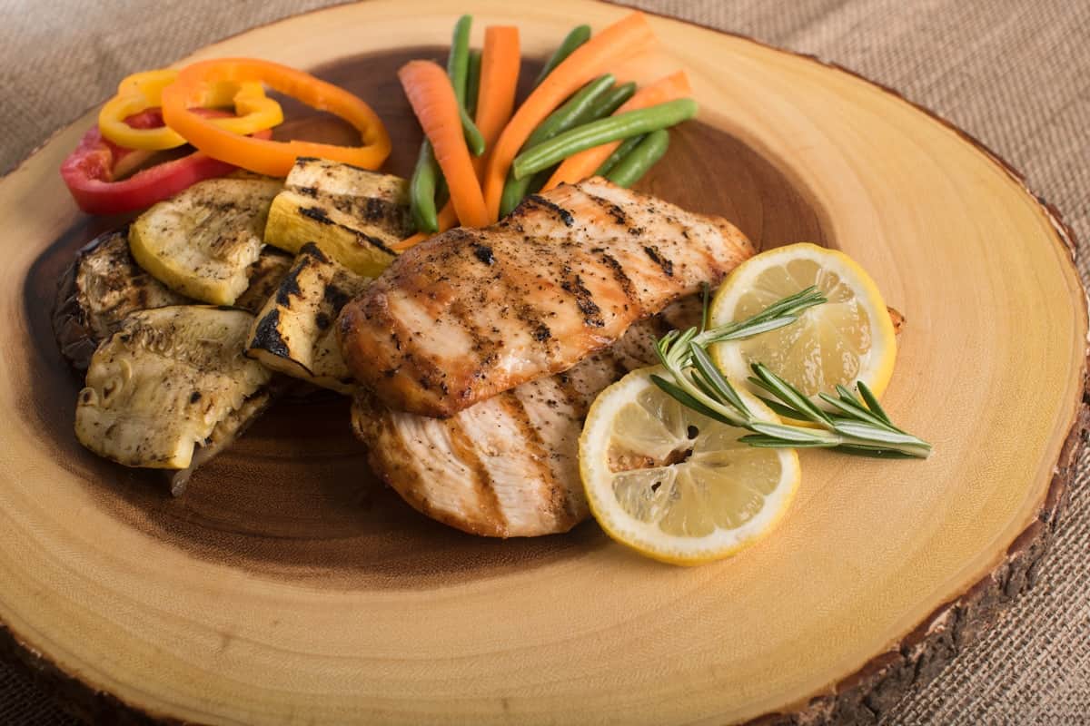Golden roasted whole chicken with crispy skin on a cutting board surrounded by fresh herbs and lemon halves