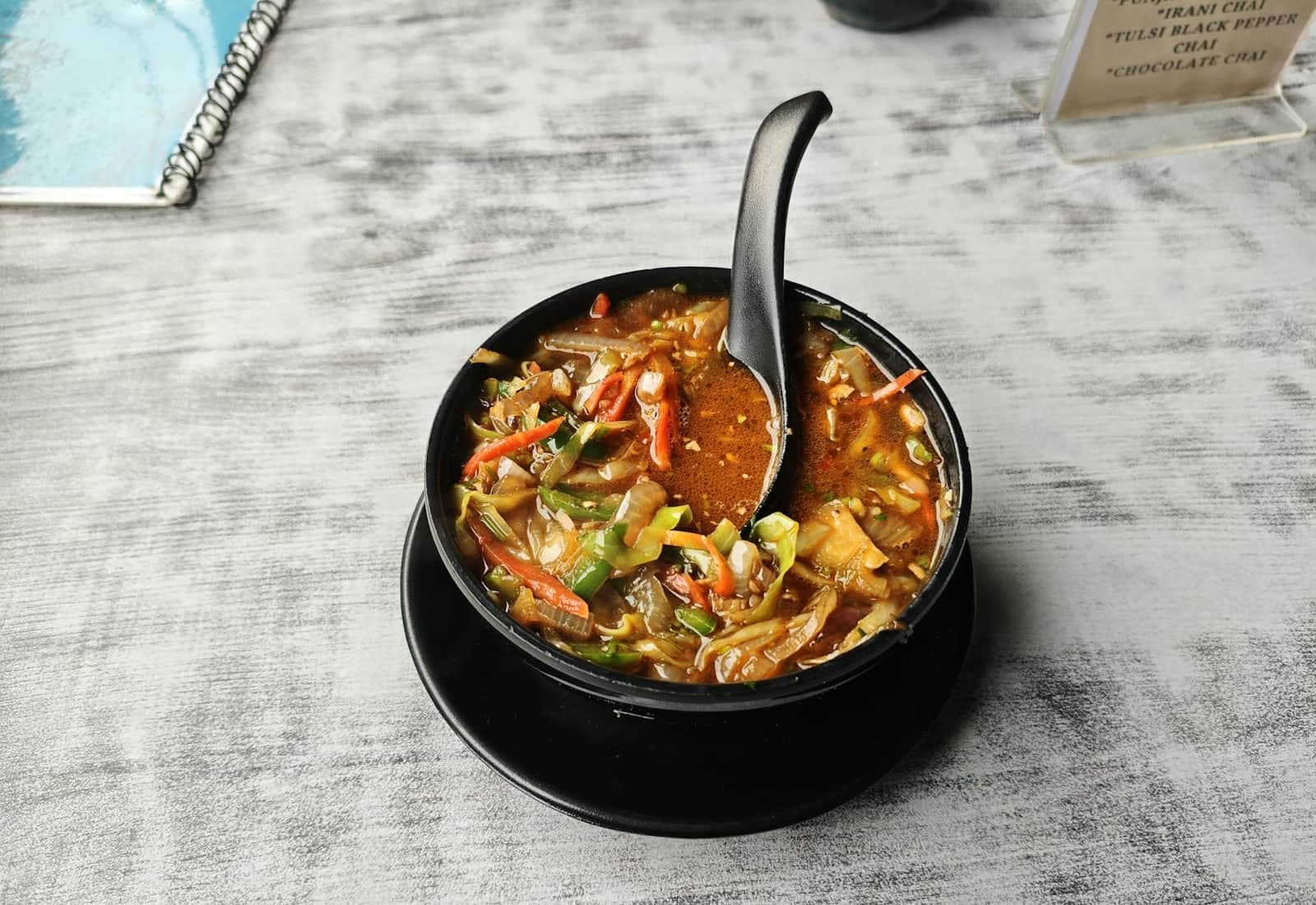 Manchow soup-style vegetable soup with noodles and vegetables in a black bowl