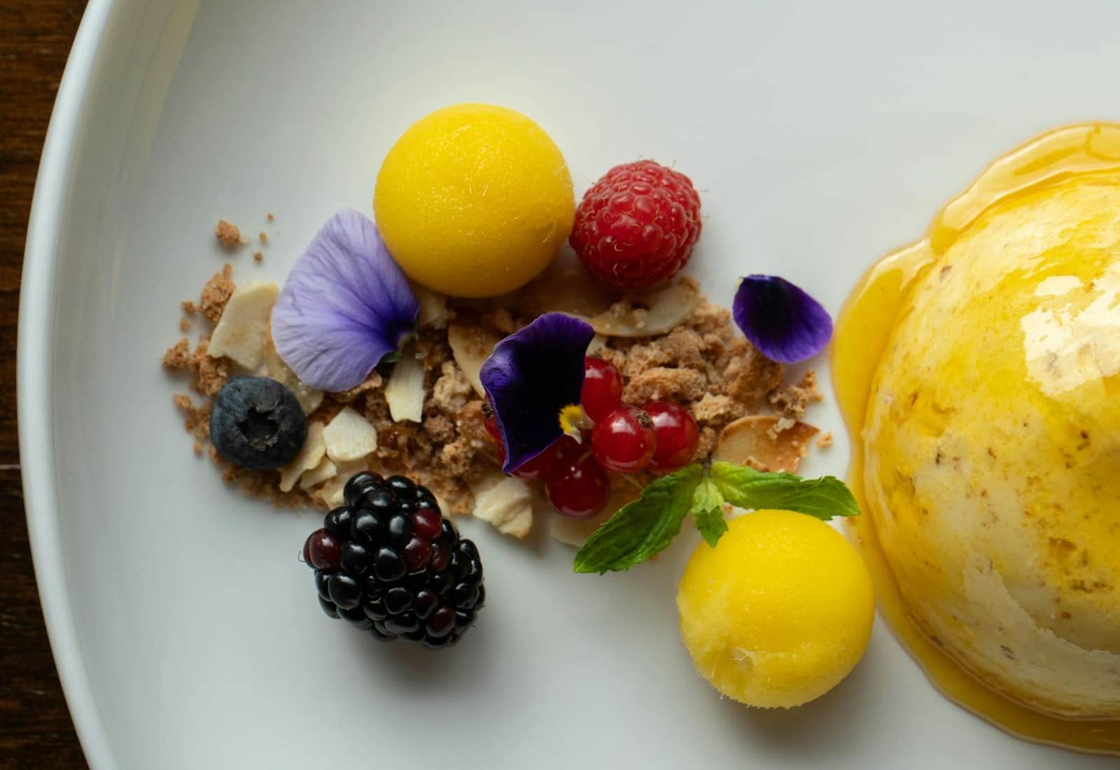 Mango sorbet dessert with bright yellow scoops, berries, and edible flowers on a plate
