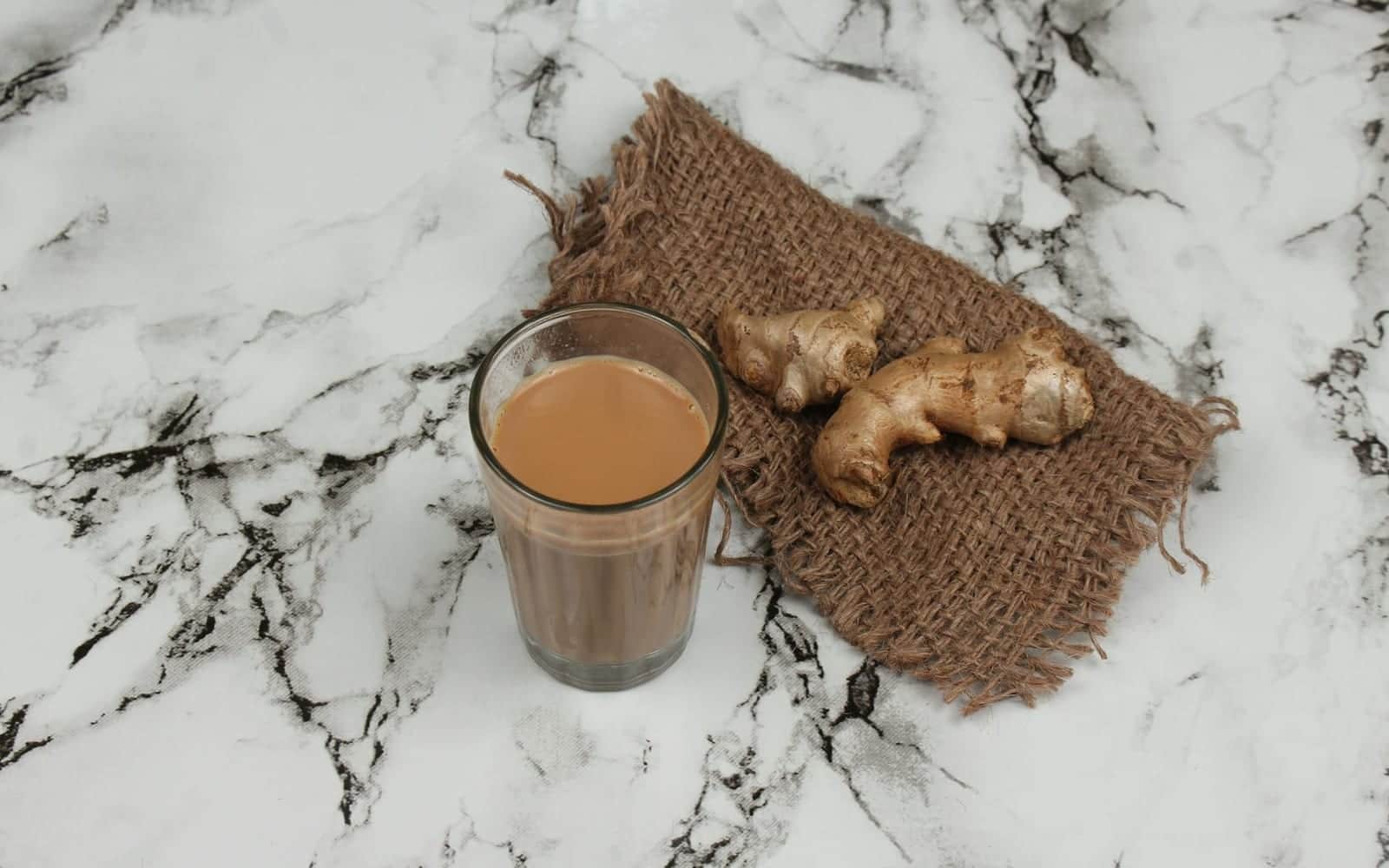 Masala chai in a glass with ginger on a marble surface