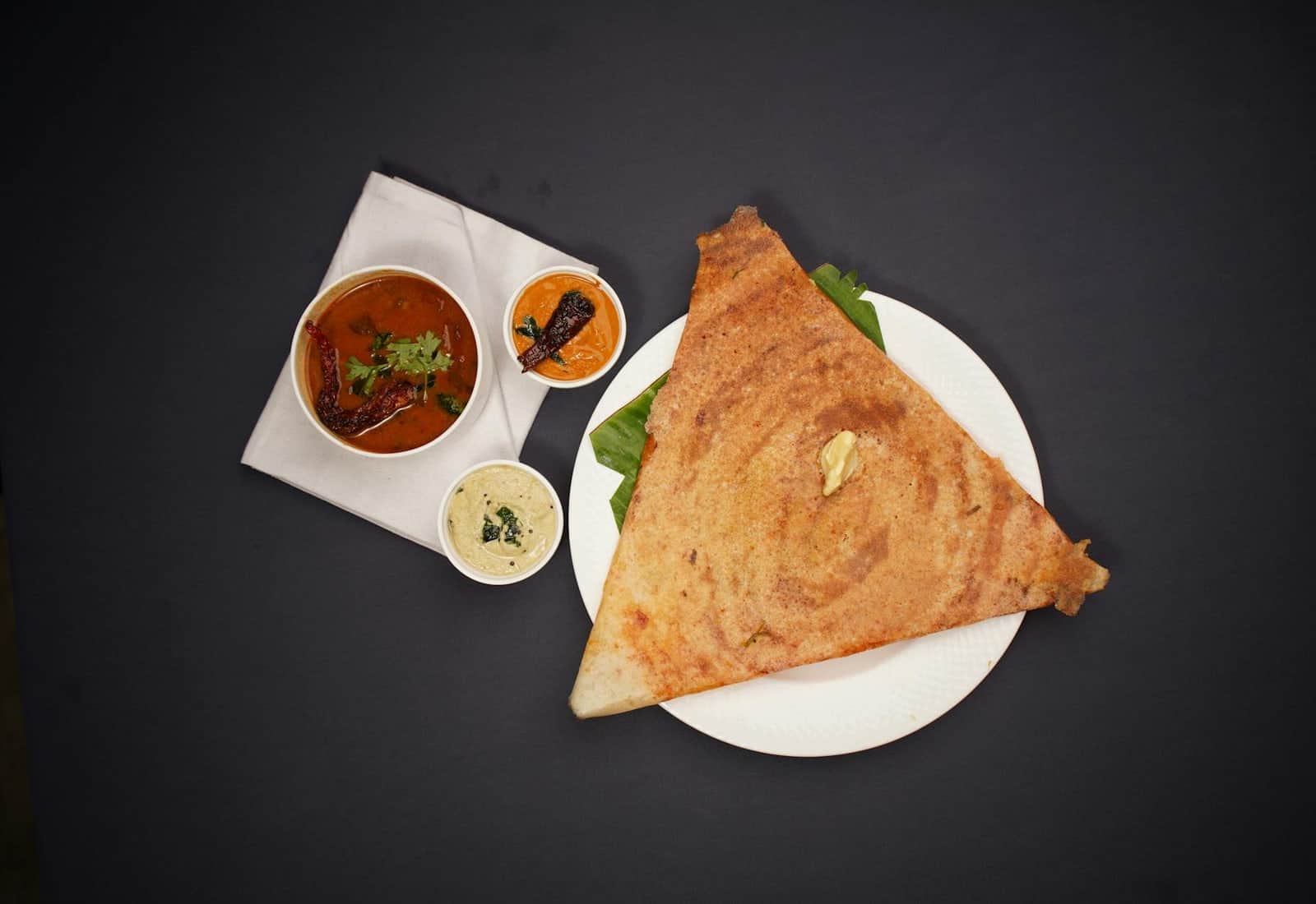 Masala dosa served with chutneys and sambar on a dark background