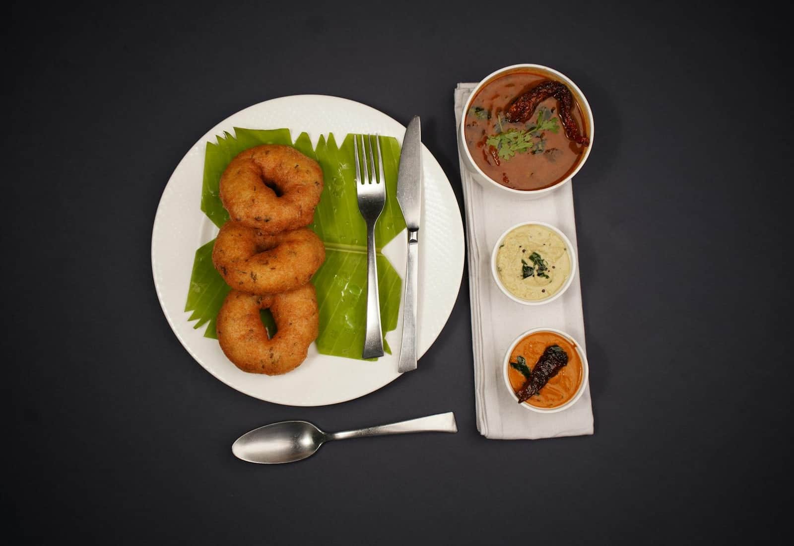 Medu vada South Indian fried lentil doughnuts served with chutneys and sambar on a black background