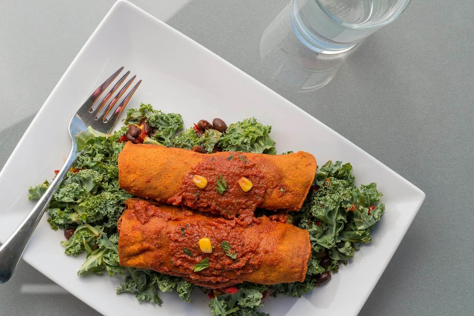 Mexican black bean enchiladas with red sauce, greens, and a fork on a plate