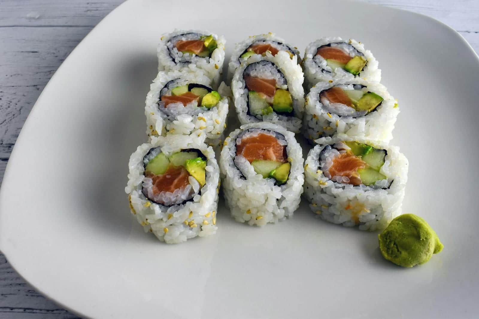 Salmon and avocado sushi rolls on a white plate with wasabi on the side