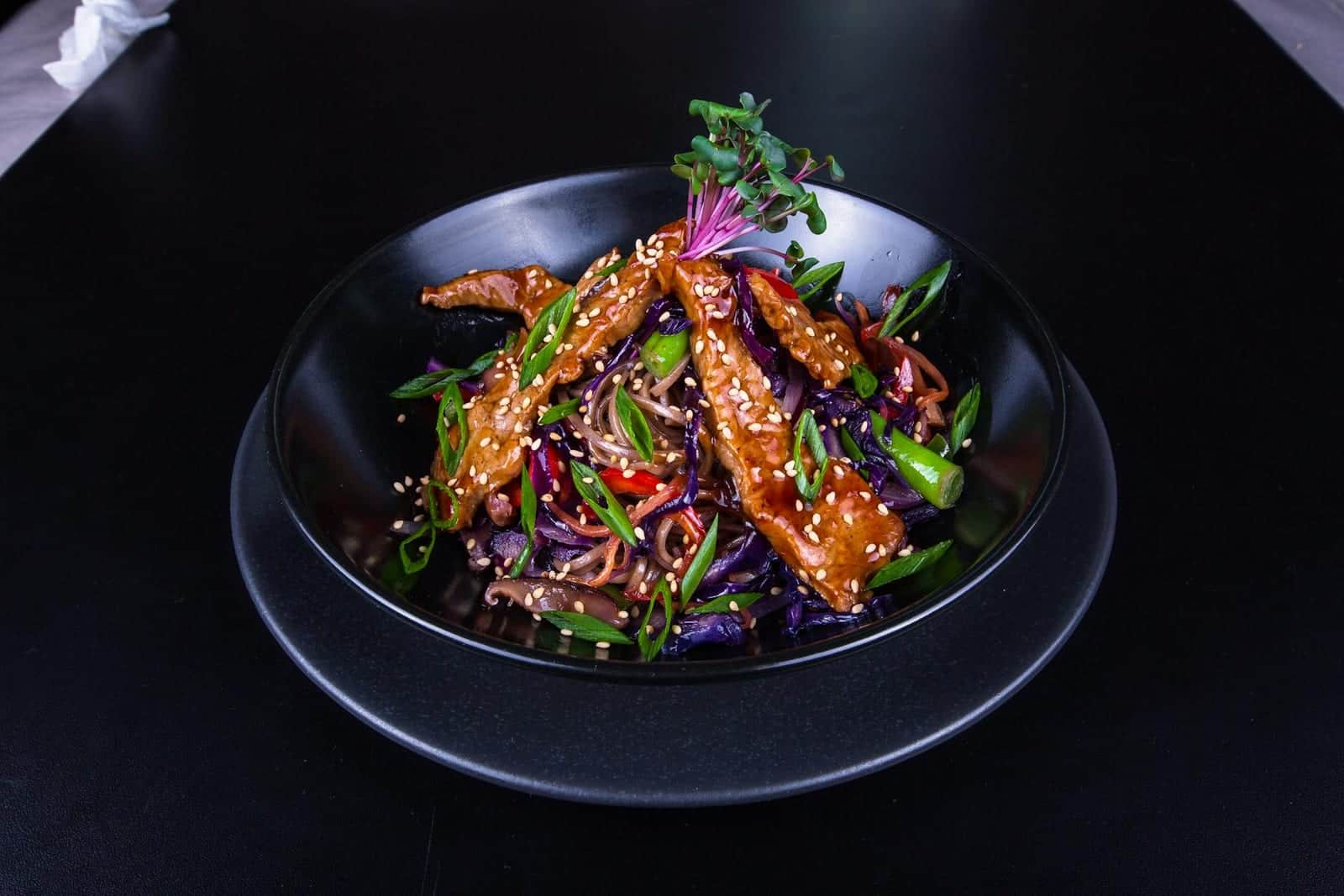 Sesame ginger chicken stir-fry with vegetables and noodles in a black bowl