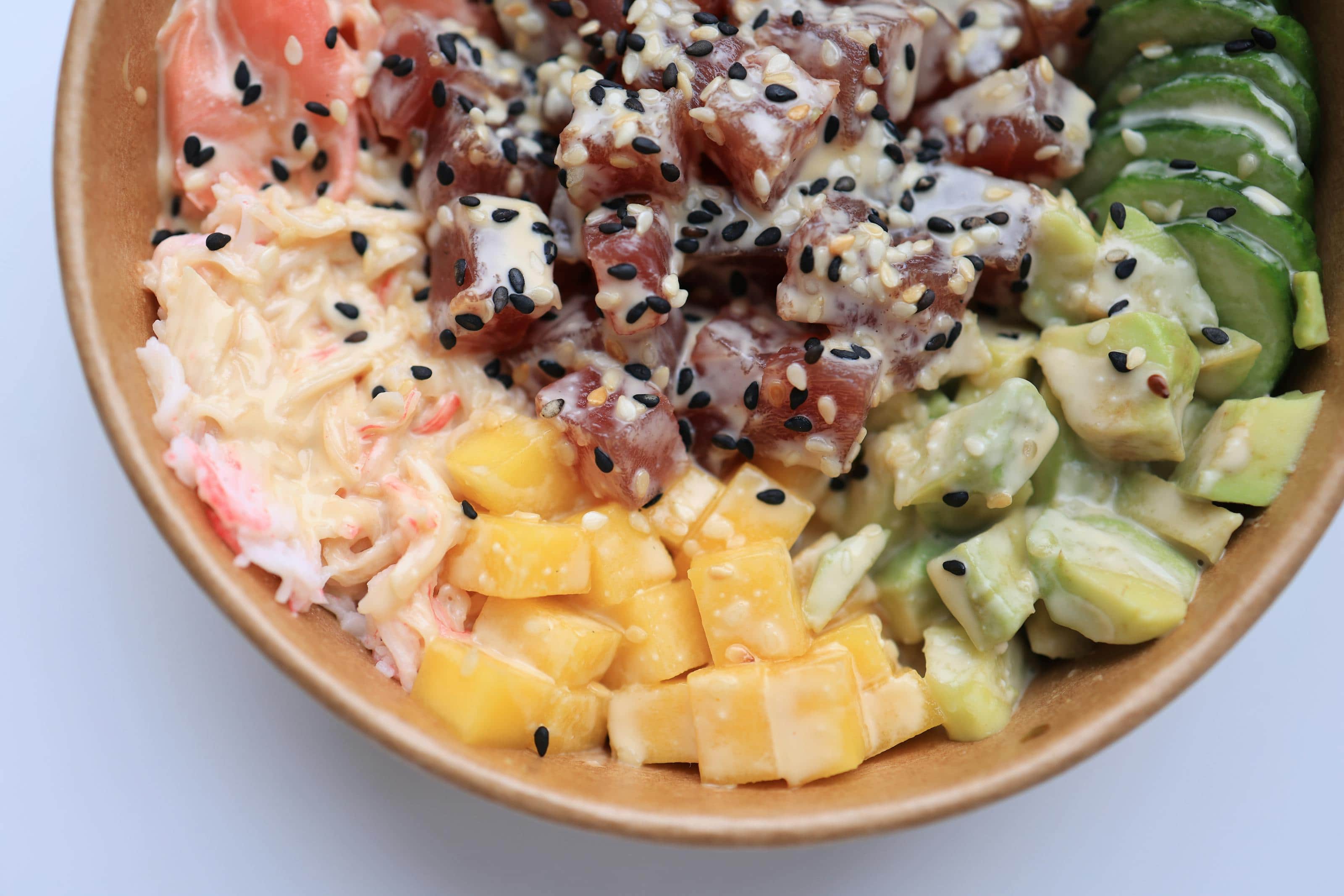 Tuna poke bowl with avocado, cucumber, mango, rice, sesame, and creamy sauce