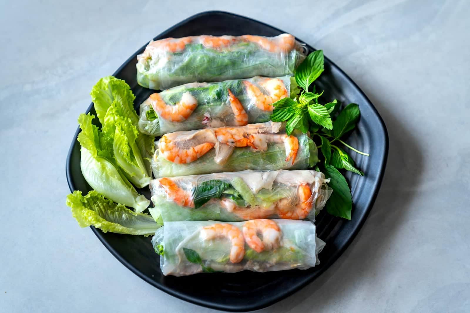 Vietnamese fresh spring rolls with shrimp, lettuce, herbs, and rice paper on a black plate