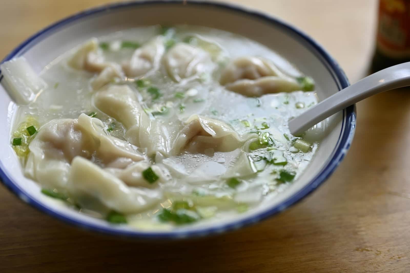Wonton soup in a blue-rimmed bowl with dumplings, clear broth, and scallions