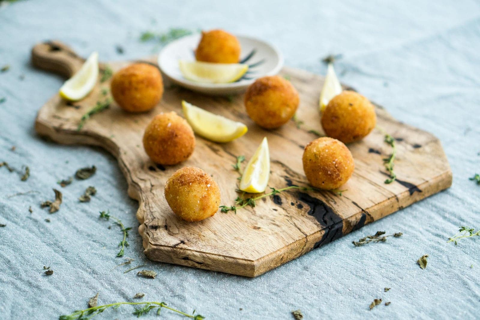 Crispy arancini risotto balls served with lime wedges and herbs on a wooden board