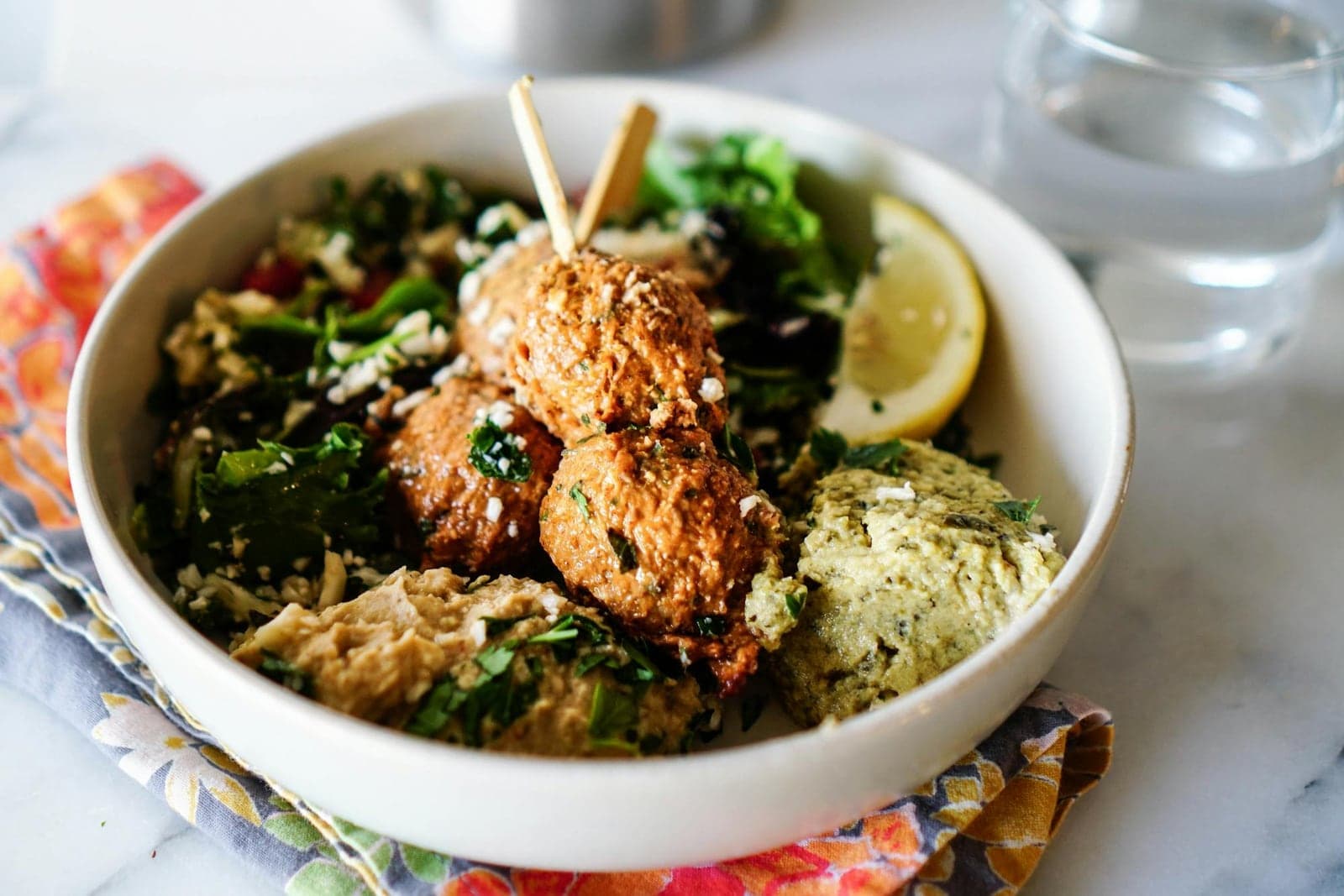 Baked falafel bowl with greens, grains, herbs, lemon, and a creamy sauce