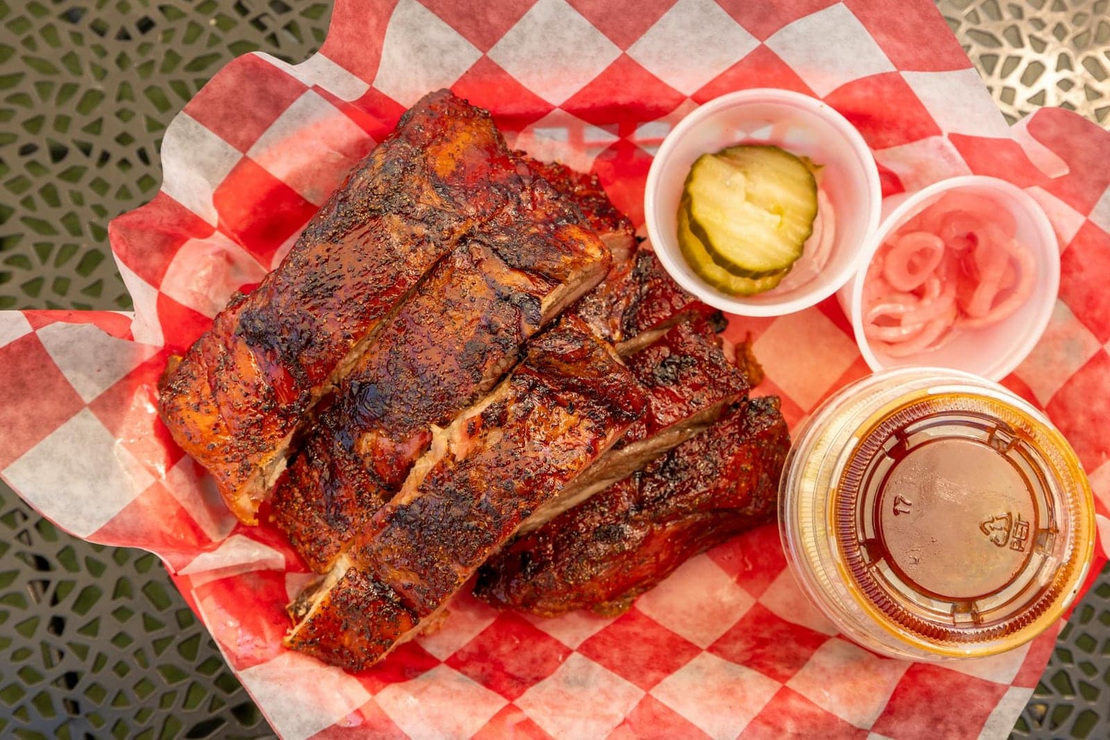 BBQ baby back ribs with sauce, pickles, and onions on red checkered paper