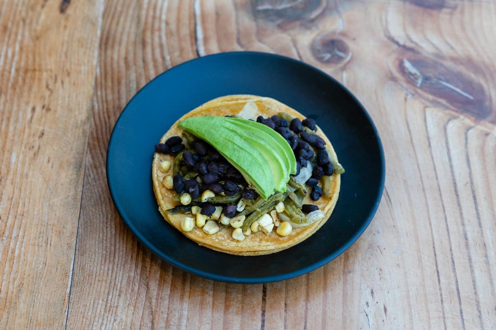 Bean and cheese tostada with avocado, black beans, corn, and cheese on a blue plate