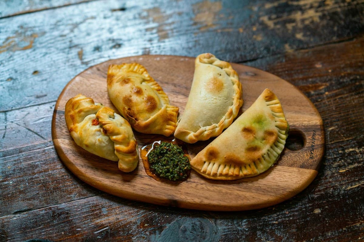 Golden beef empanadas with green chimichurri sauce on a wooden board