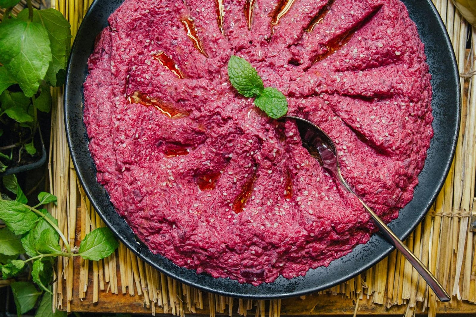 Beet hummus in a bowl with olive oil, mint, and a deep pink color