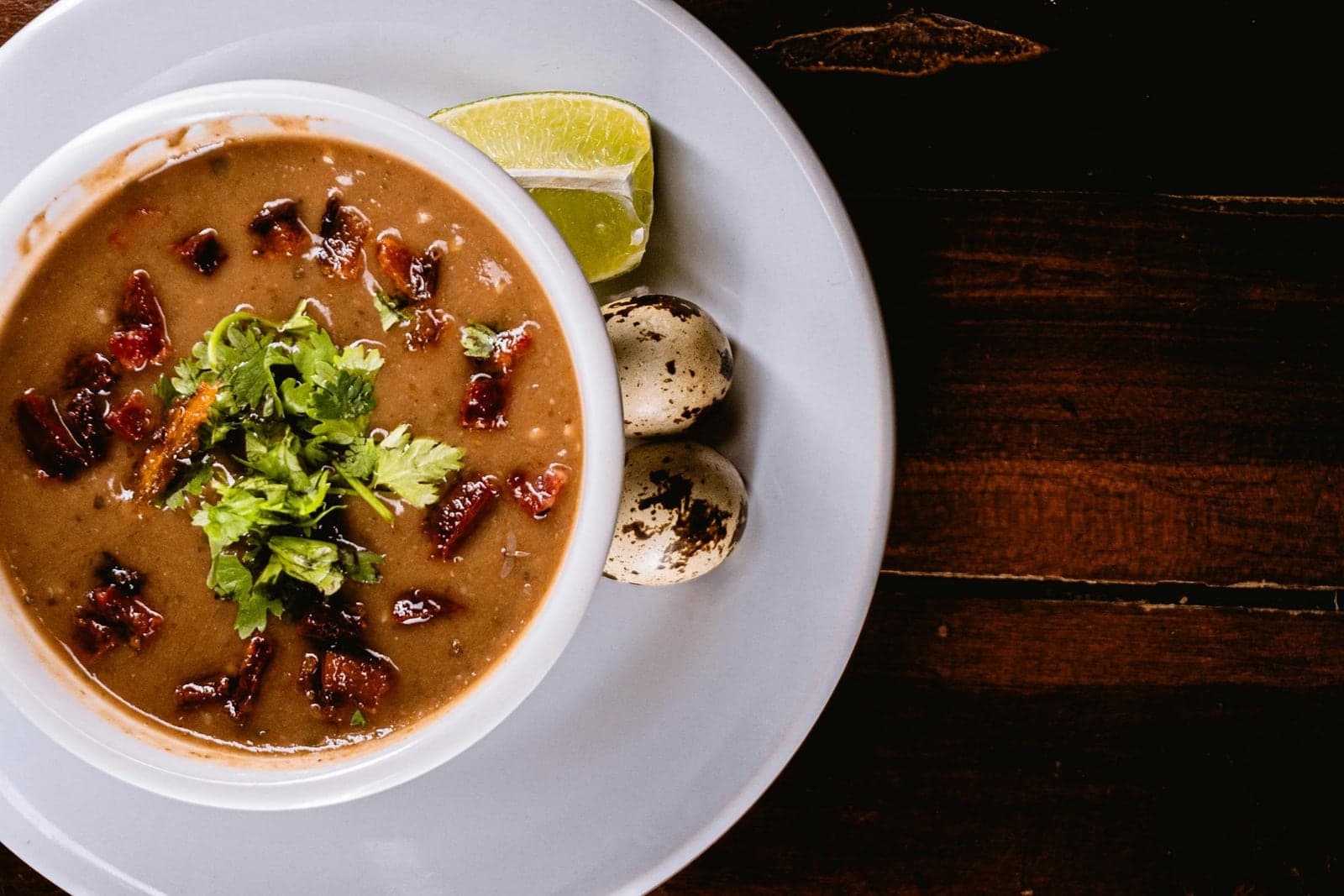 Mexican black bean soup garnished with herbs, lime, and crema in a shallow bowl