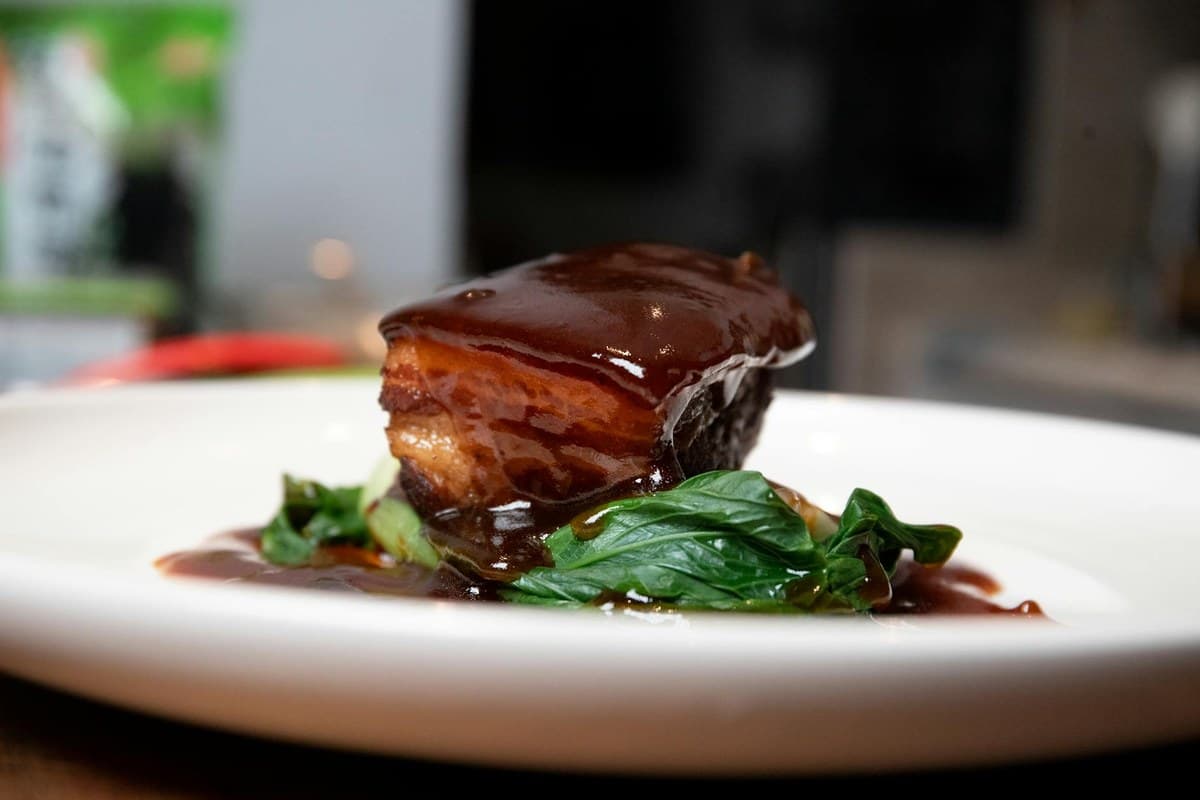 Braised pork belly with glossy sauce and greens on a white plate