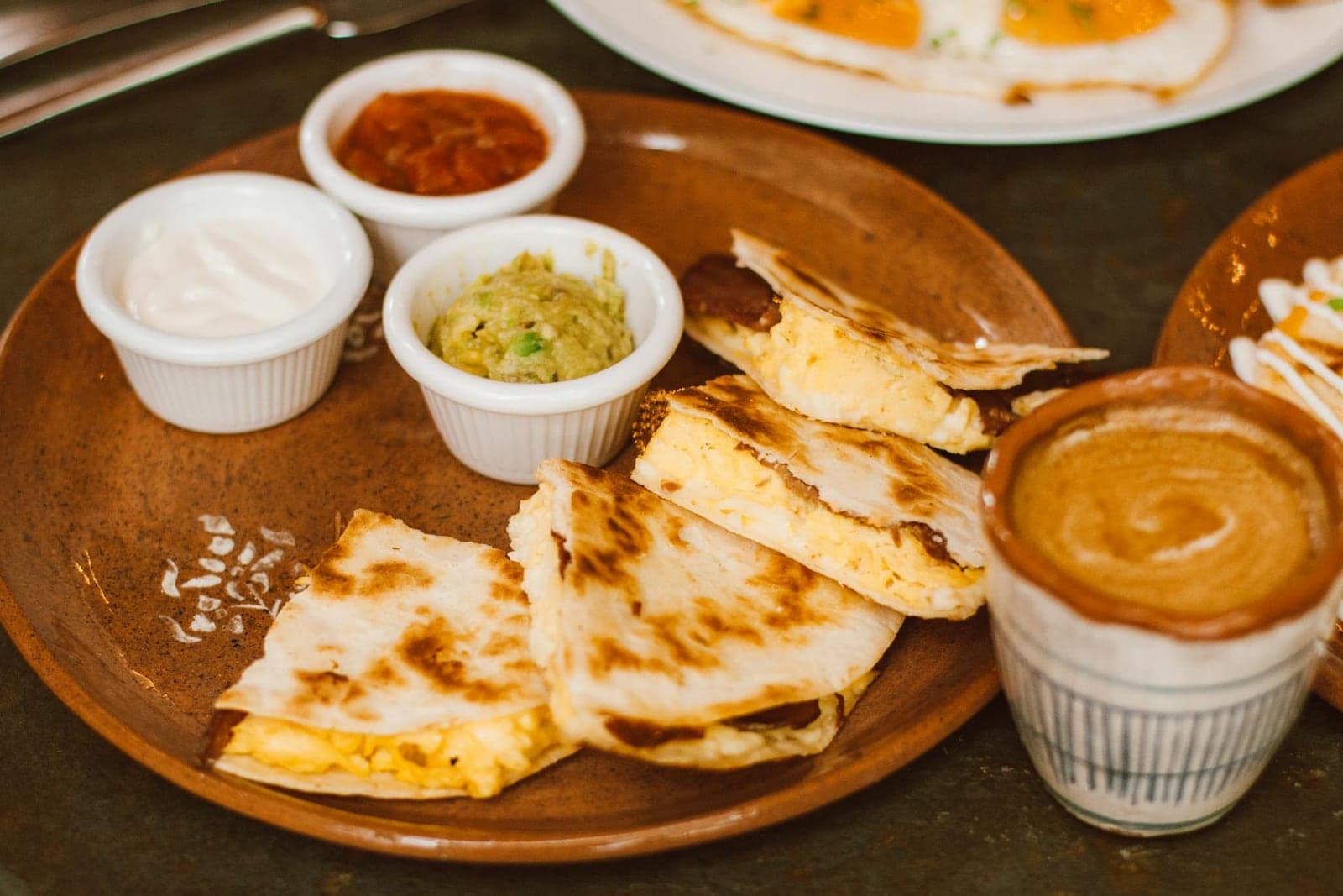 Breakfast quesadilla wedges with salsa, guacamole, crema, and eggs on a wooden platter
