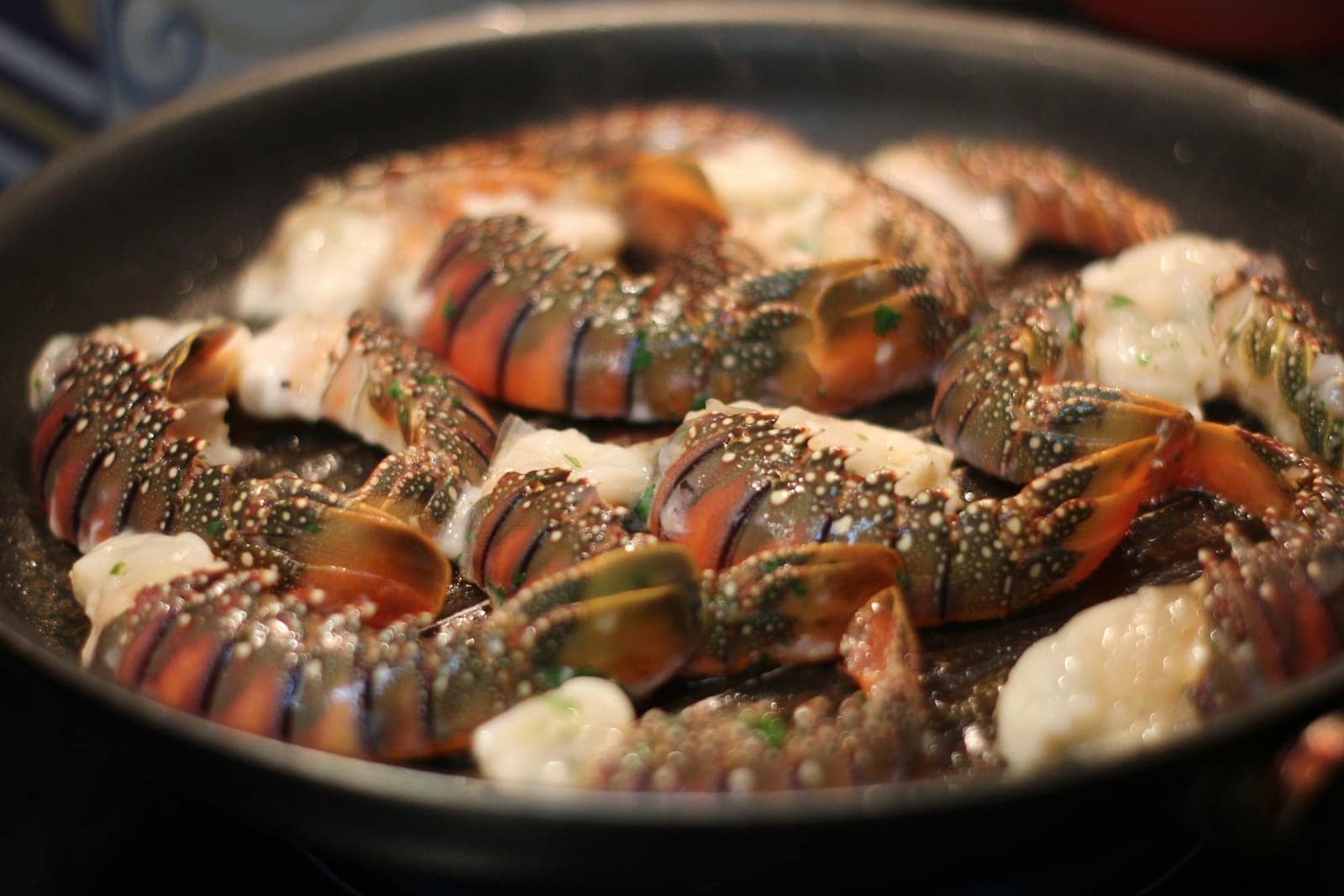 Broiled lobster tails with garlic butter and herbs sizzling in a pan