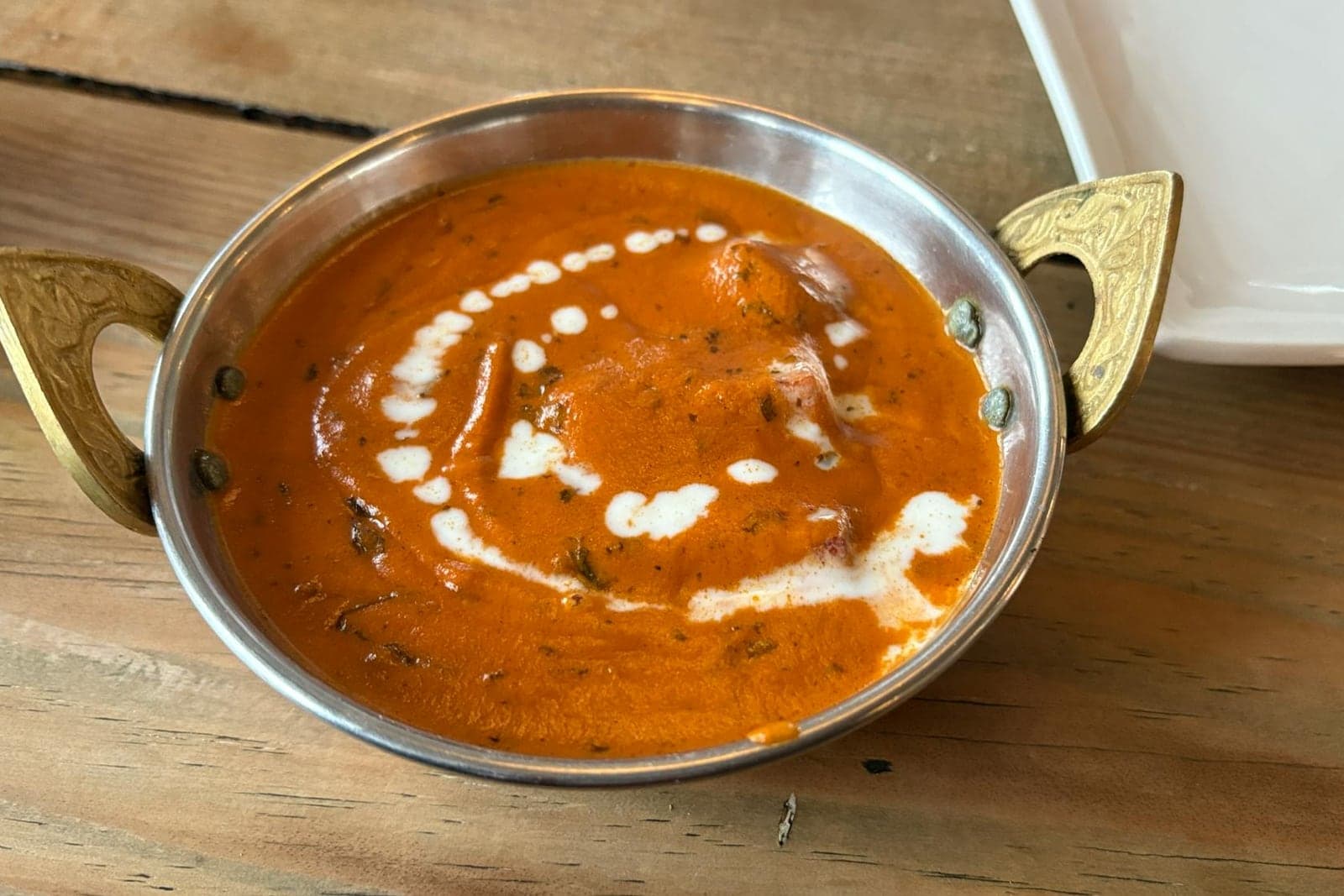Butter chicken in creamy orange curry sauce served in a brass bowl