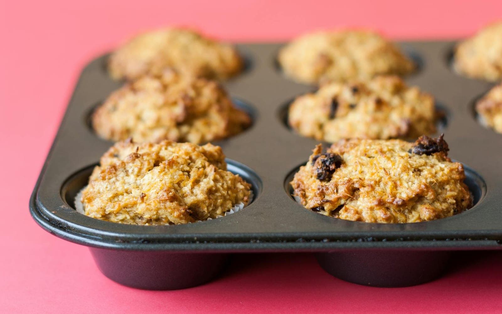 Carrot cake muffins for kids baked in a muffin tin on a pink surface