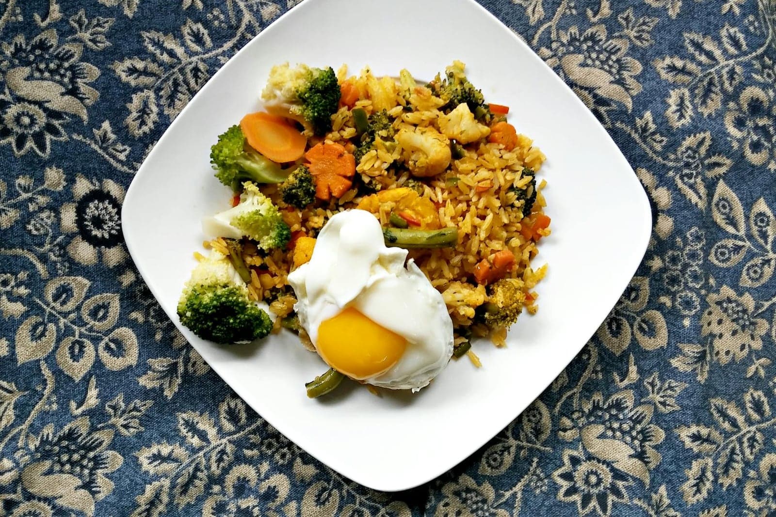 Cauliflower fried rice with vegetables, broccoli, carrots, and a fried egg on a white plate