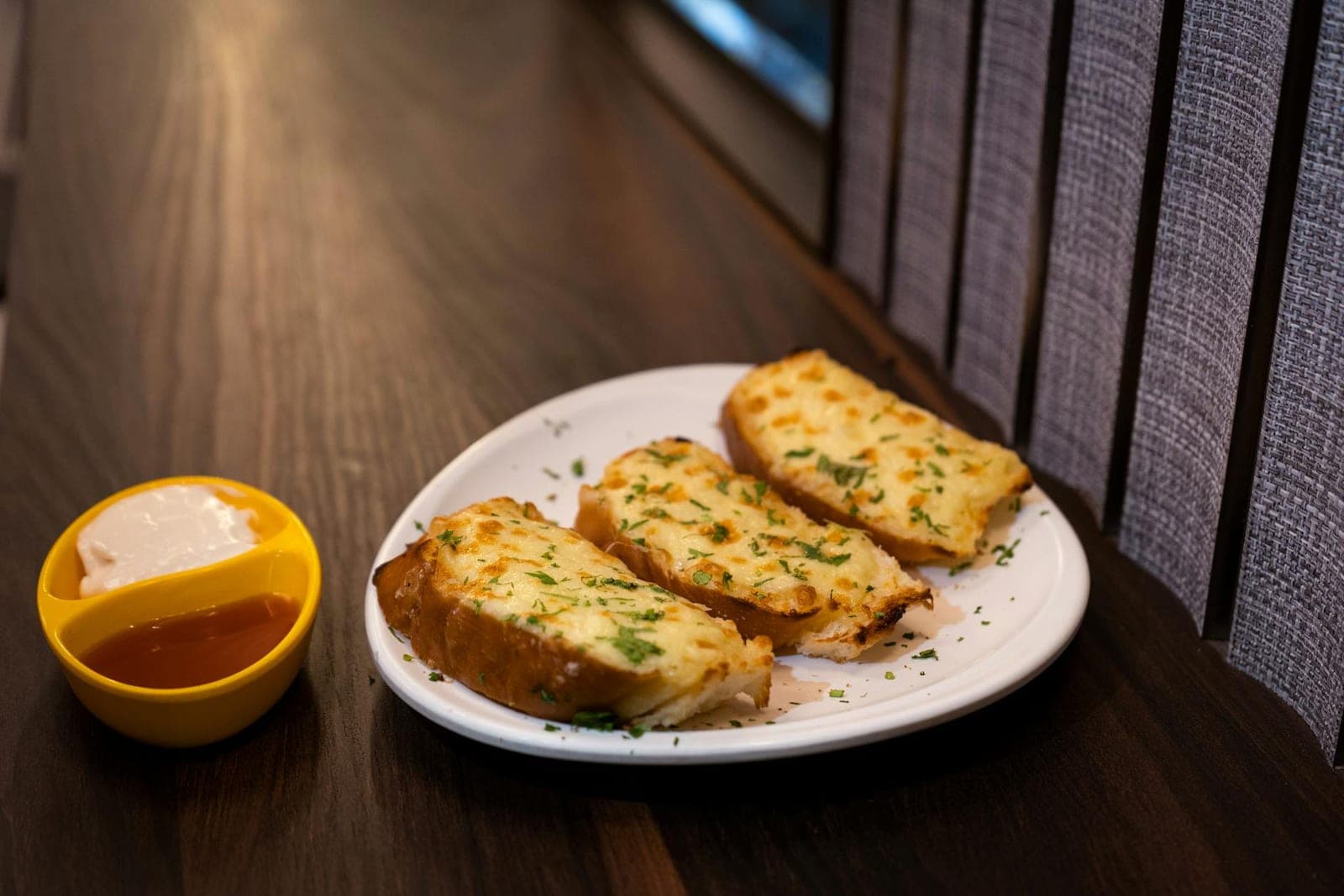 Cheesy garlic bread slices with herbs and a dipping sauce on a white plate