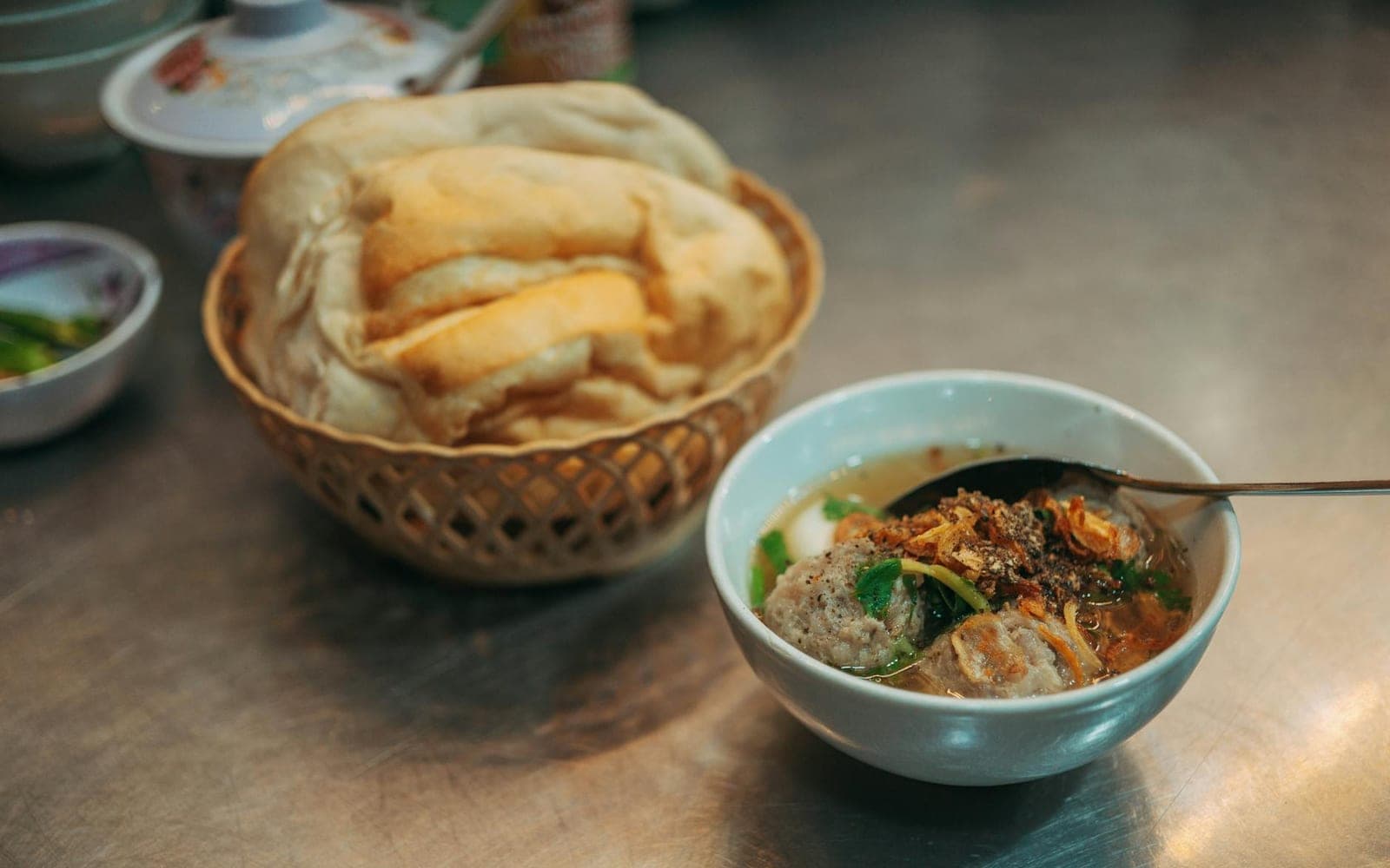Chicken meatball soup in a bowl with broth, herbs, and bread nearby