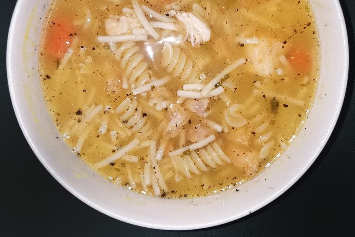 A bowl of classic chicken noodle soup with egg noodles, shredded chicken, carrots, and celery in golden broth