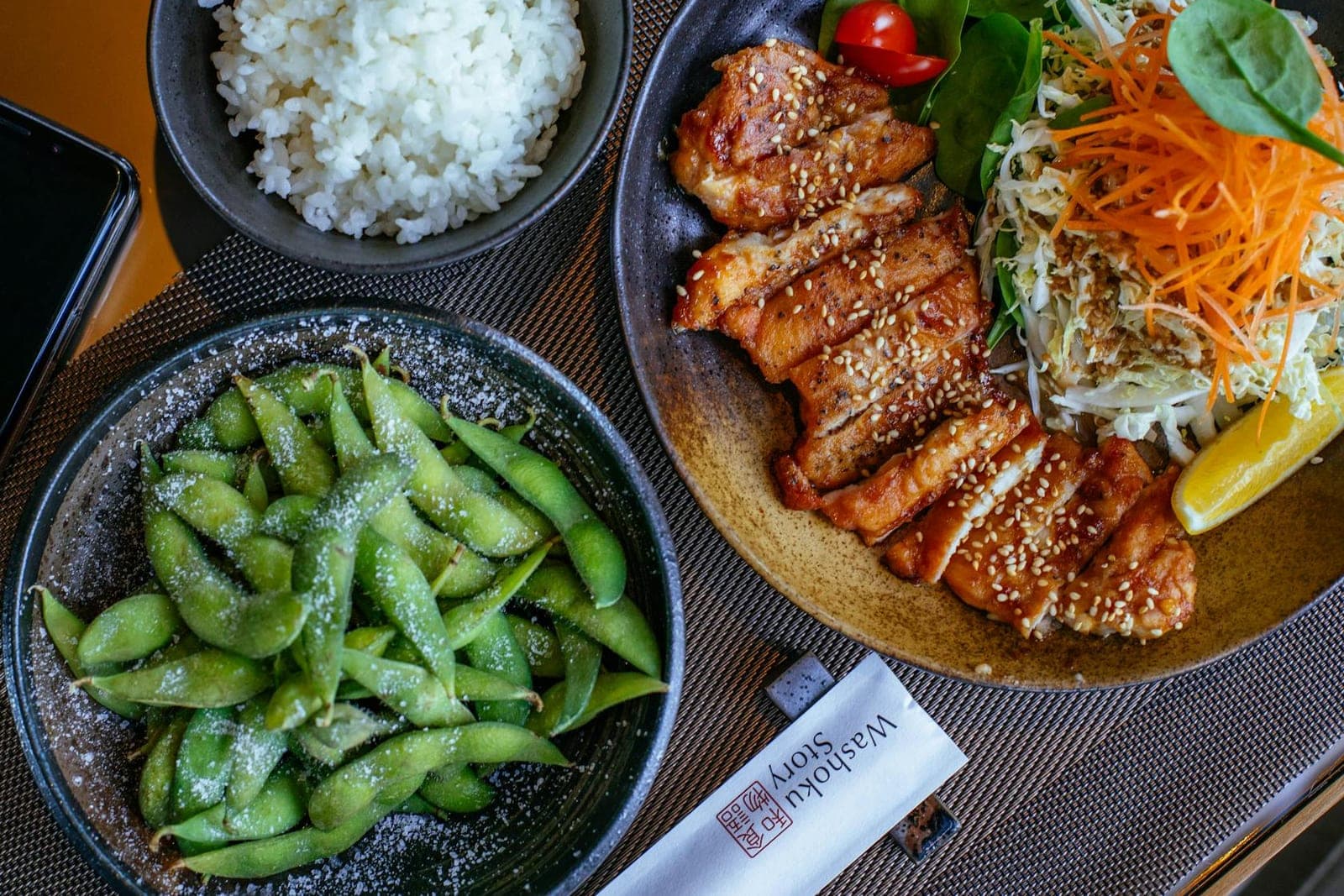 Chicken teriyaki with rice, edamame, vegetables, and glossy sauce in Japanese bowls