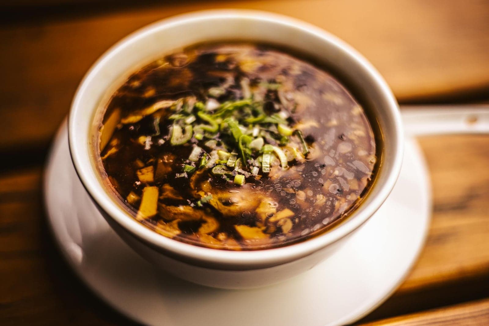 Chinese hot and sour tofu soup in a bowl with dark broth, tofu, mushrooms, and scallions