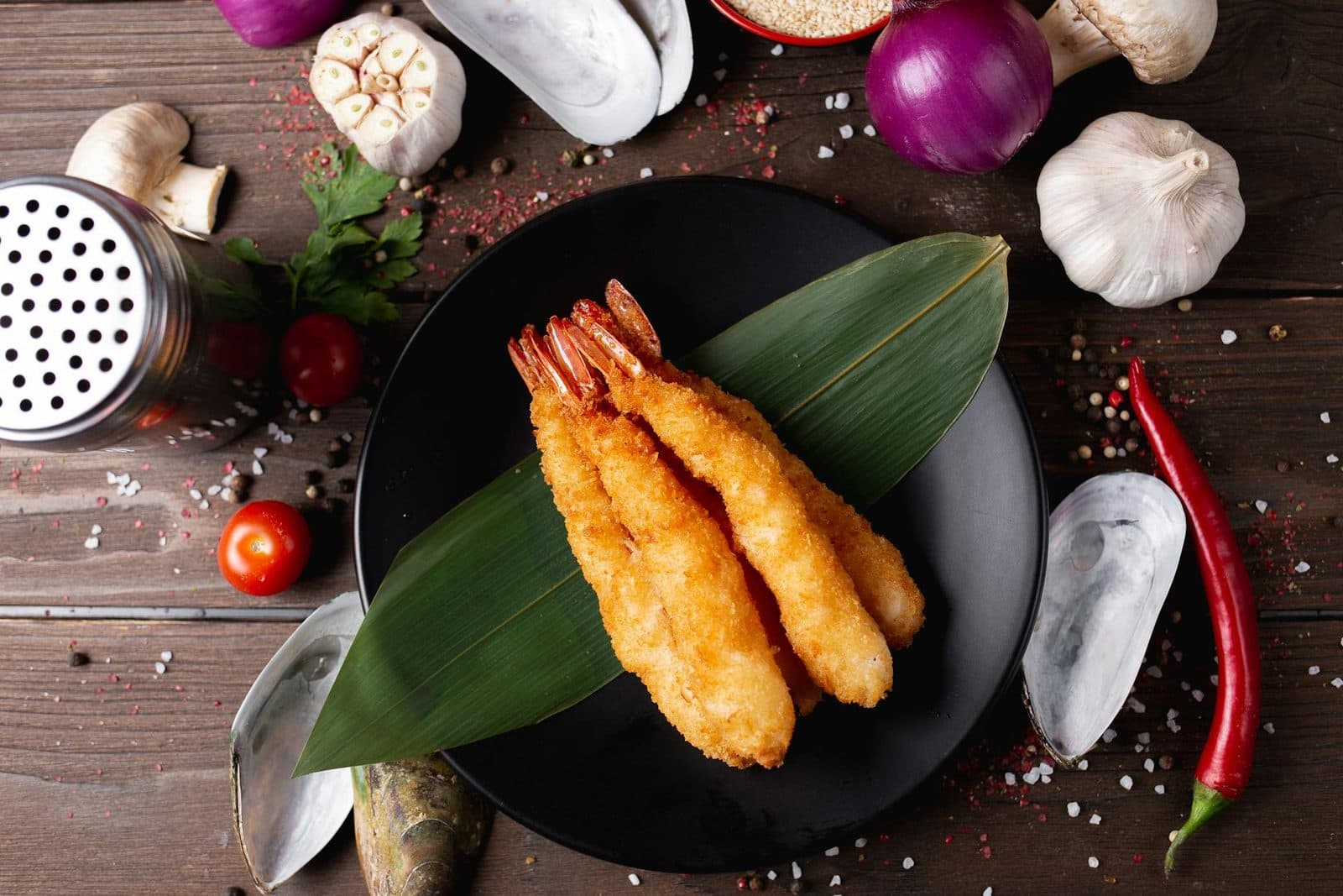 Chinese salt and pepper shrimp fried crisp with garlic, tomatoes, and spices on a black plate