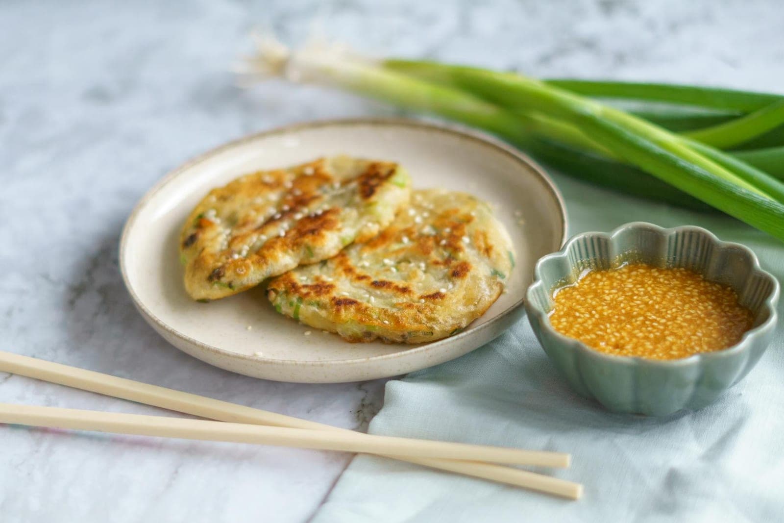 Chinese scallion pancakes with dipping sauce, chopsticks, and scallions on the side