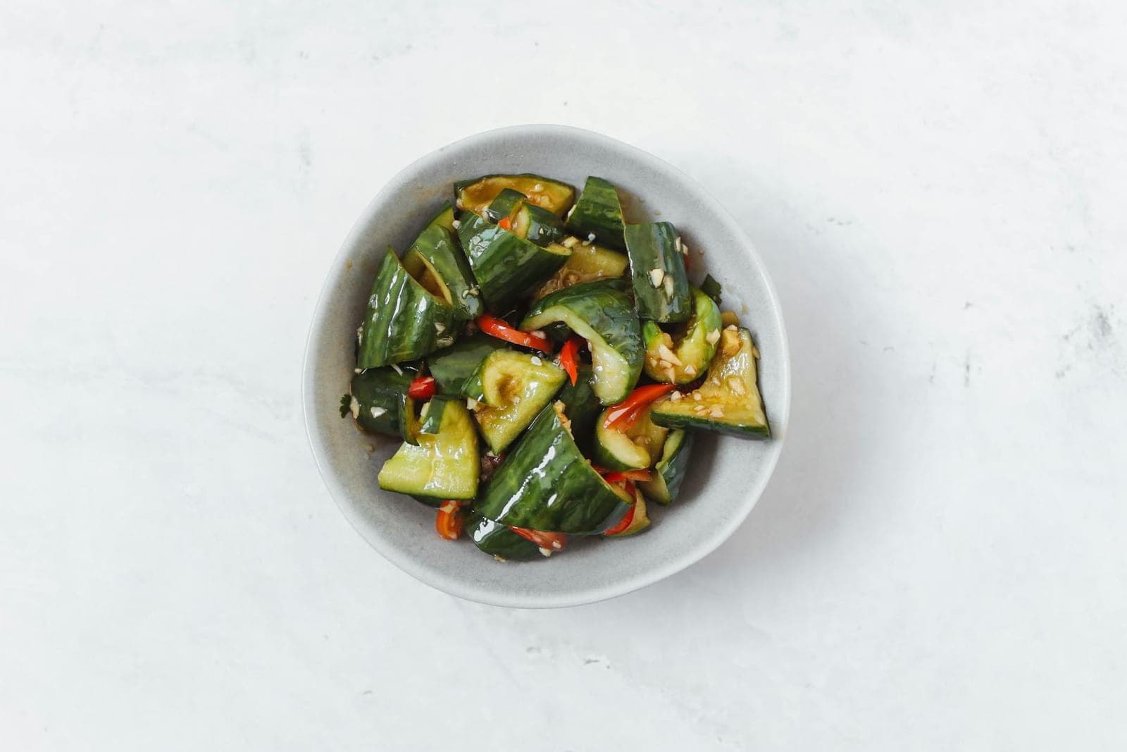 Chinese smashed cucumber salad with cucumber chunks, peppers, and dressing in a white bowl